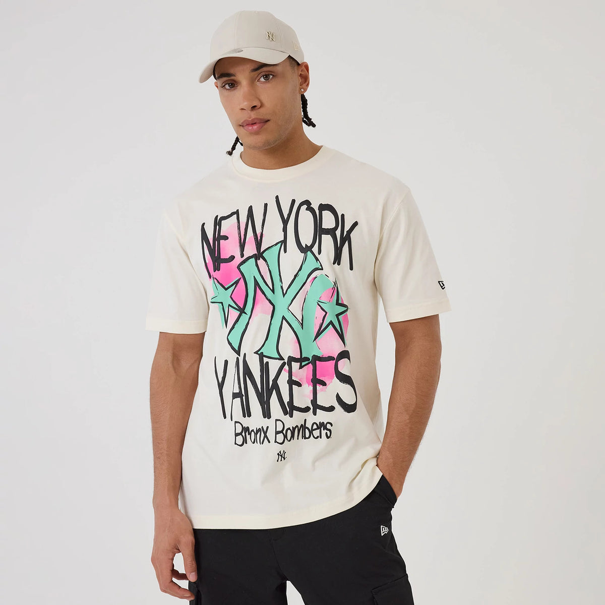New Era New York Yankees MLB Street Art Graphic Light Beige T-Shirt, front view on-model displaying a graphic design with green, pink, and black elements, New York Yankees lettering across the chest, small embroidered New Era logo on the sleeve.