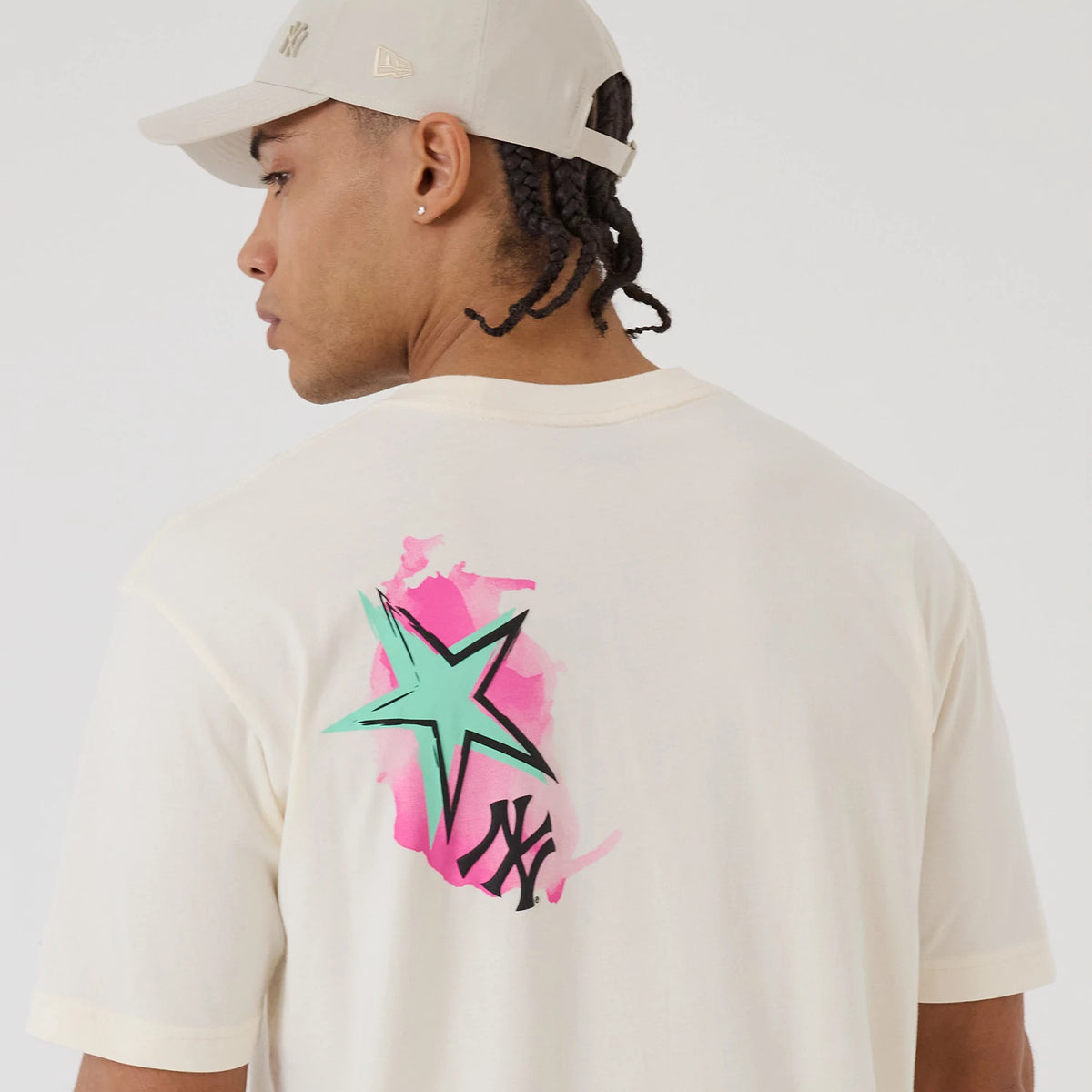 New Era New York Yankees MLB Street Art Graphic Light Beige T-Shirt, back view on a model wearing a matching beige cap, featuring a large green star over a pink splash and a black Yankees logo near the bottom right.