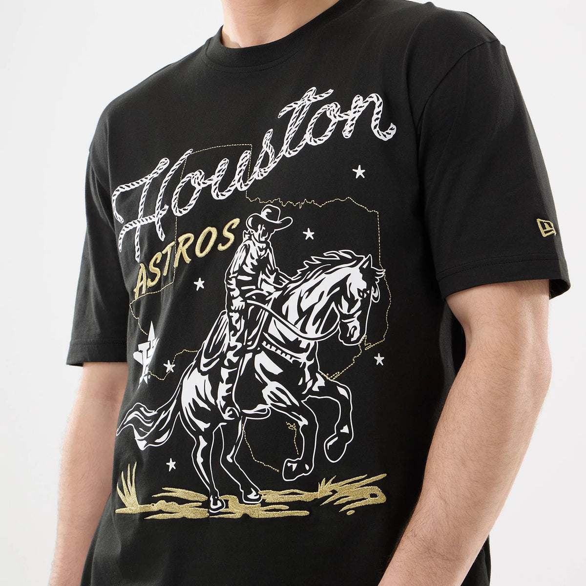 New Era Houston Astros MLB Cowboy Graphic Black T-Shirt, front view showing an intricate graphic of a cowboy on horseback with Houston across the chest, small white stars, Astros in gold lettering and an embroidered New Era logo on the left sleeve.