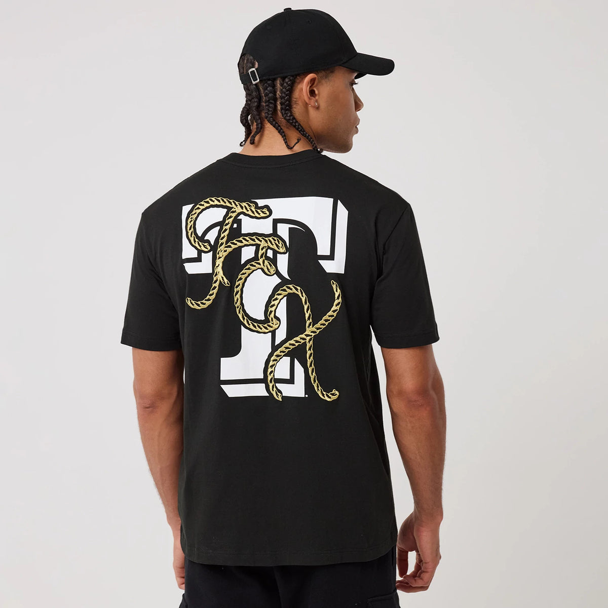 New Era Texas Rangers MLB Cowboy Graphic Black T-Shirt, back view showing a large white letter T with yellow rope forming the letters F and C across the back, worn by a model with a black cap.