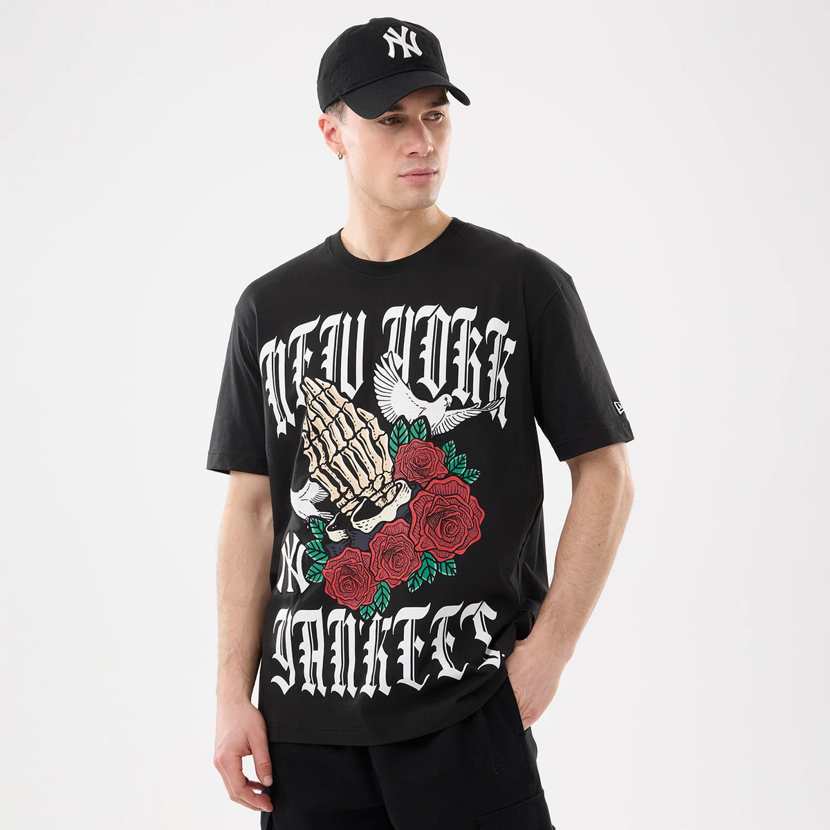 New Era New York Yankees MLB Script Graphic Black T-Shirt, front view on a model highlighting a graphic of praying hands, roses, and doves with white lettering saying New York Yankees and an embroidered New Era logo on the sleeve.
