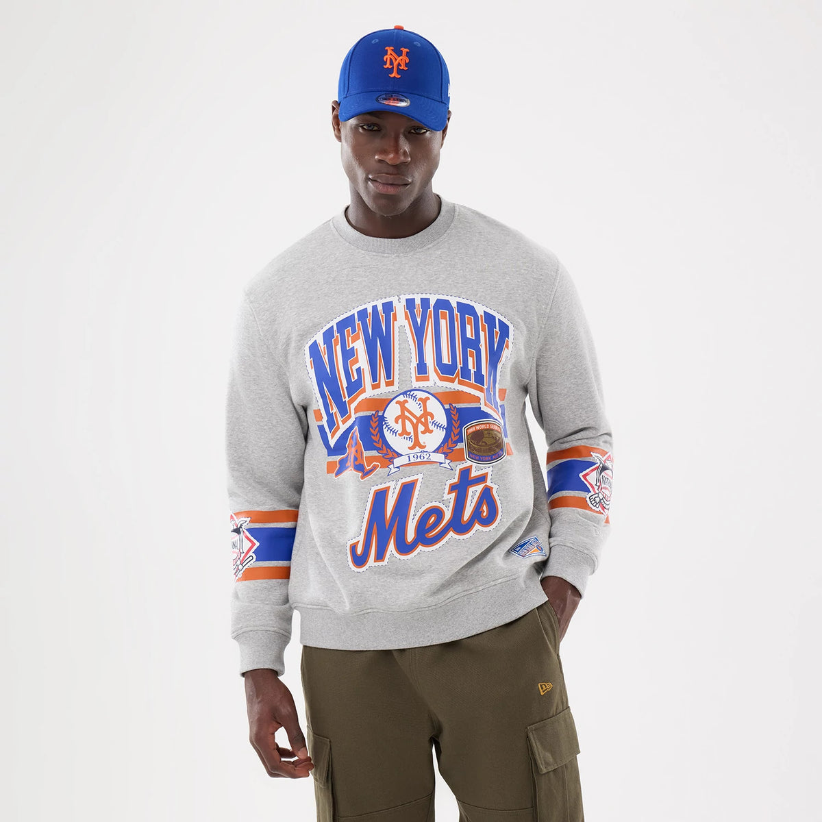 New Era New York Mets MLB Sport Classic Grey Crew Neck Sweater, front view on a model showing large New York Mets graphics across the chest with additional team logos on both sleeves and a ribbed collar and cuffs.