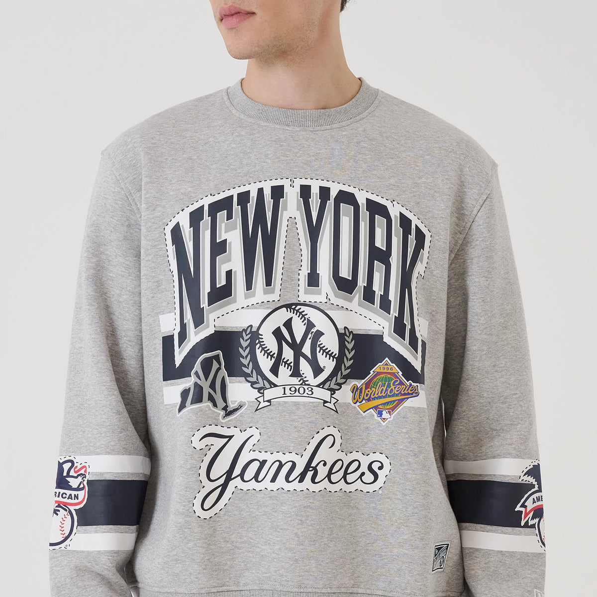 New Era New York Yankees MLB Sport Classic Grey Crew Neck Sweater, front view on a model featuring large New York Yankees graphics across the chest, detailed World Series and NY logos, and striped sleeves with additional team patches.