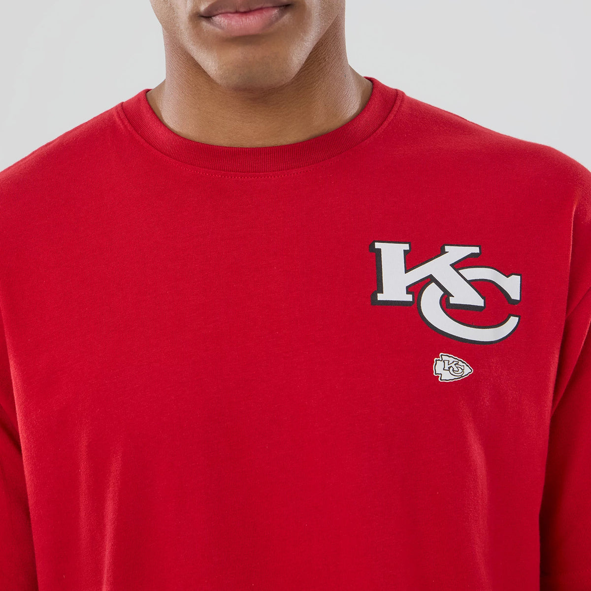 New Era Kansas City Chiefs NFL Graphic Red T-Shirt, front view showing a large white and grey KC logo printed on the left chest with a smaller team emblem below, displayed on a model wearing the red shirt.