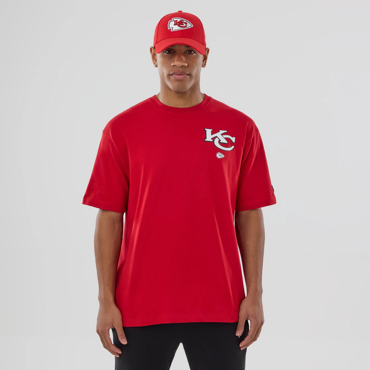 New Era Kansas City Chiefs NFL Graphic Red T-Shirt, front view on-model showing a K-C logo in raised print on the left chest, the red design paired with a matching red cap featuring an embroidered Chiefs logo.