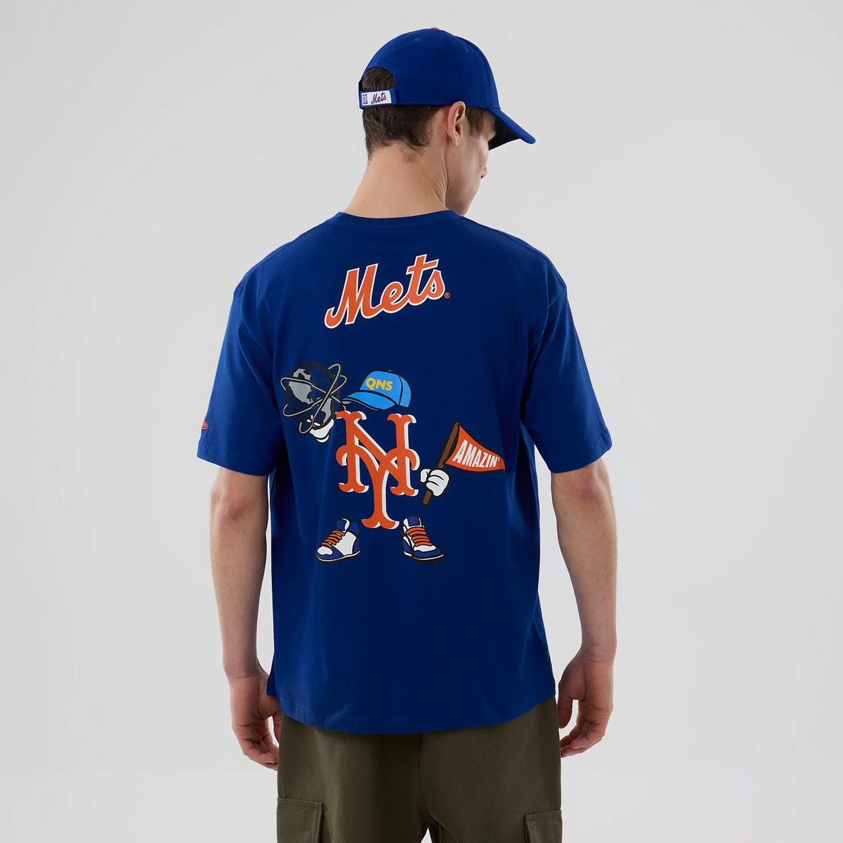 New Era New York Mets MLB Graphic Blue T-Shirt, back view on a model with a Mets cap, featuring Mets lettering at the top and a playful graphic of the team logo cartoon character holding a megaphone and wearing trainers and a hat.