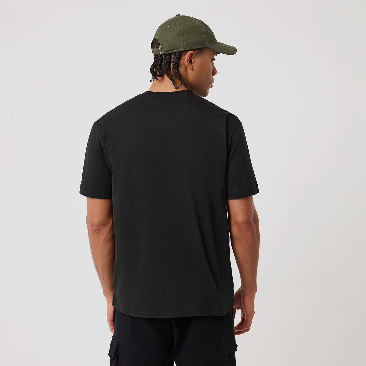 New Era LA Dodgers MLB Script Graphic Black T-Shirt, back view on-model showing a plain black back with a straight hem, styled with dark cargo shorts and a green cap featuring matching eyelets.