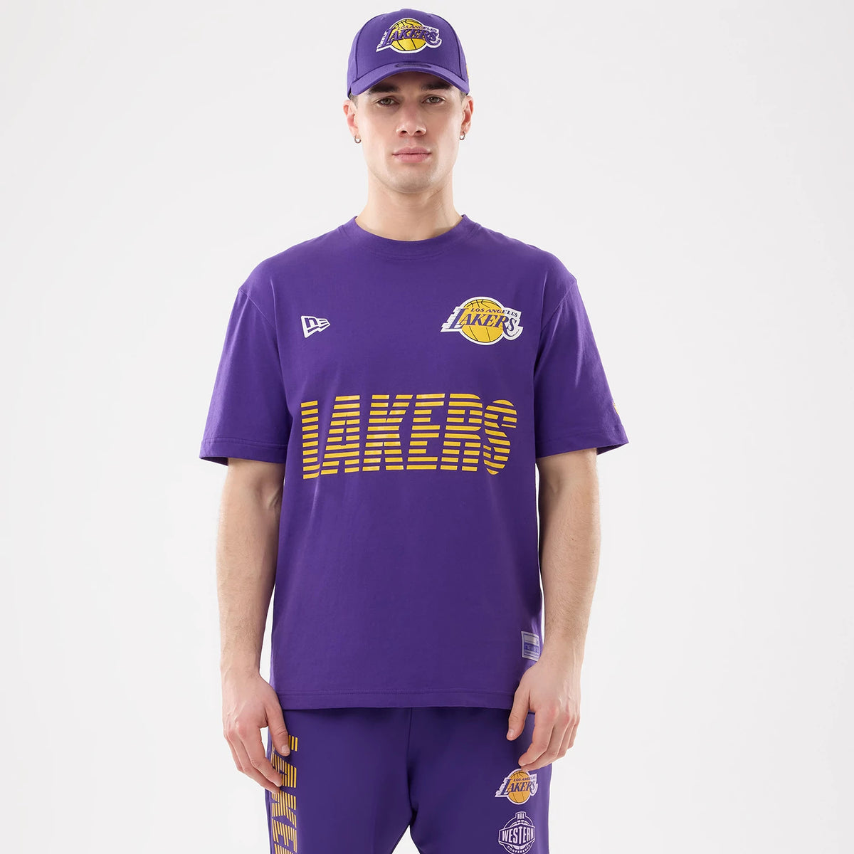 New Era LA Lakers NBA Match Purple T-Shirt, front view on-model showing the yellow Laker lettering and logo across the chest, a white embroidered New Era logo on the upper right chest, styled with matching purple shorts.