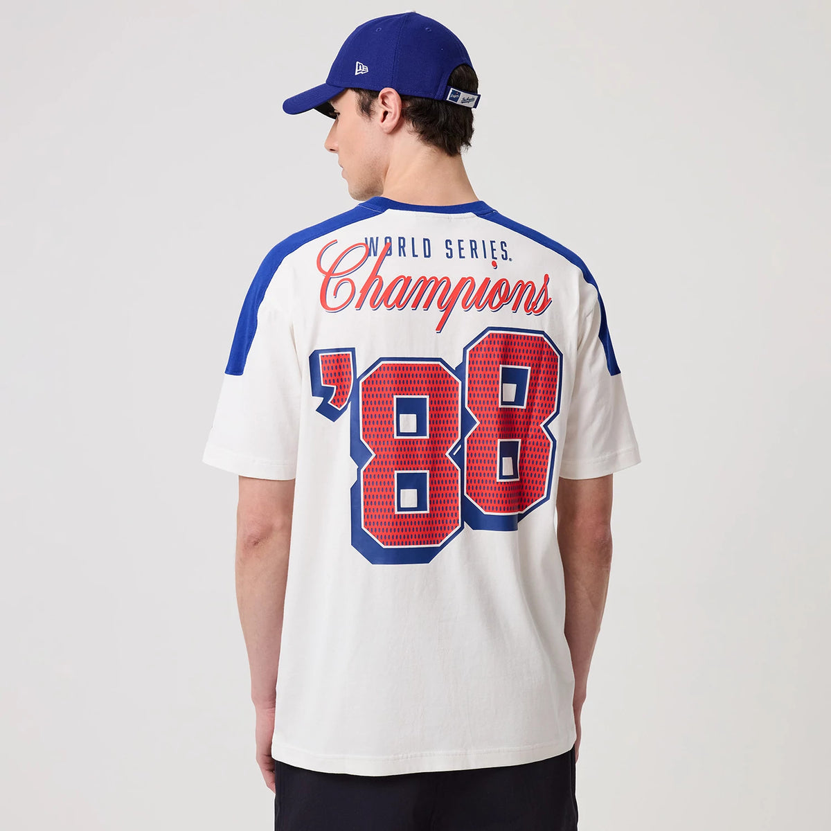 New Era LA Dodgers MLB Sport Classic White T-Shirt, back view on a model with a blue cap, featuring World Series Champions in red script and large grid-patterned '88 in blue and red on the white fabric with blue shoulder accents.