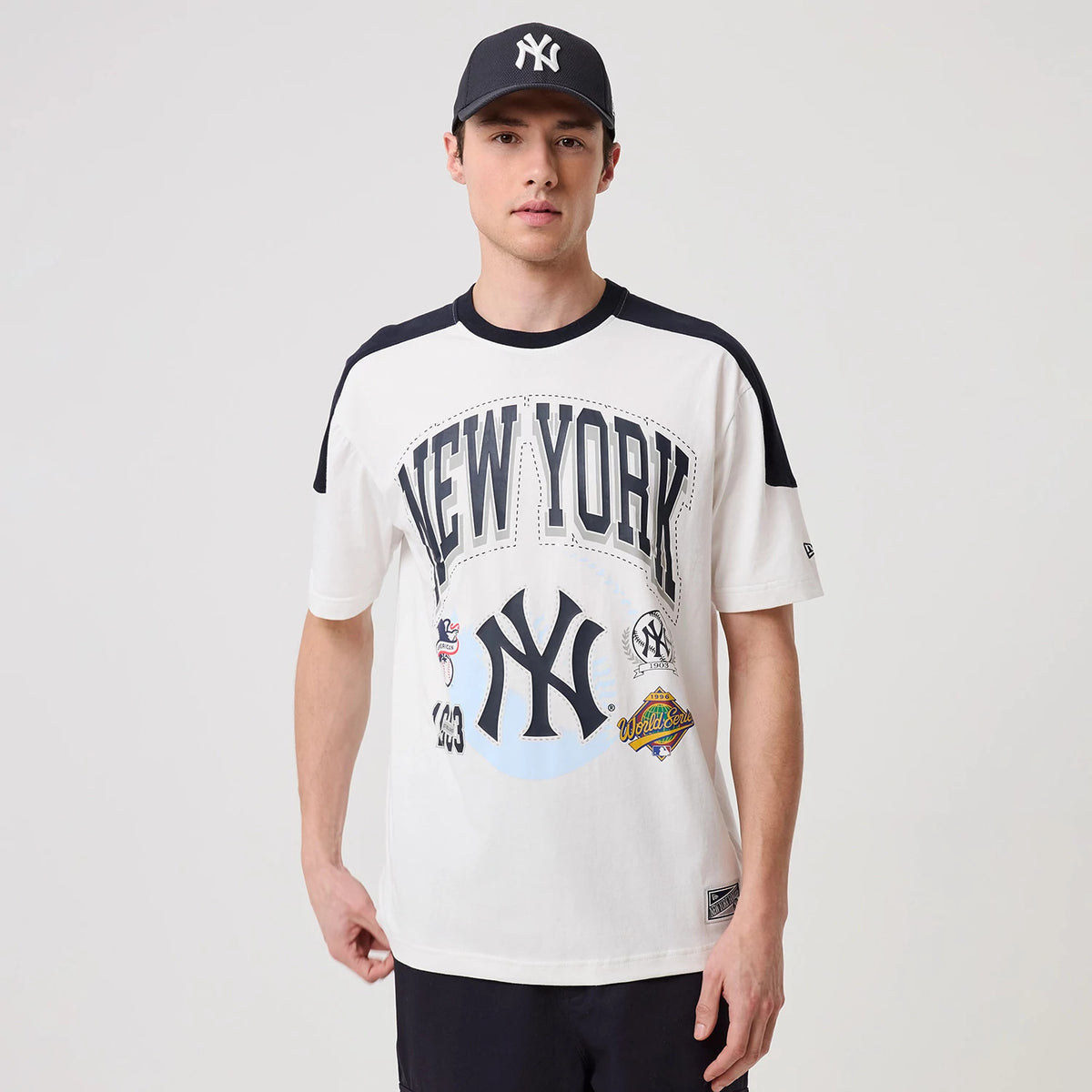 New Era New York Yankees MLB Sport Classic World Series White T-Shirt, front view on-model featuring large printed New York lettering across the chest, Yankees logo below, and colourful World Series patches near the hem.