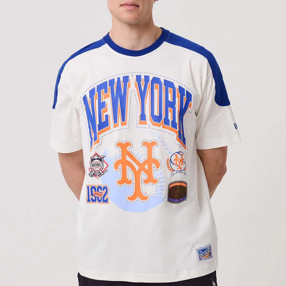 New Era New York Mets MLB Sport Classic White T-Shirt, front view on-model features large blue and orange New York text and logo across the chest, team emblems and 1962 lettering below, with contrasting blue sleeves and collar detail.