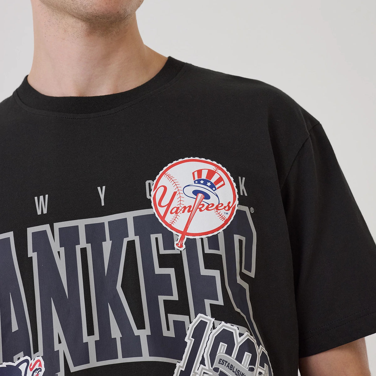 New Era New York Yankees MLB Sport Classic Black T-Shirt, front view showing grey Yankees lettering across the chest, a large printed Yankees logo with stars and a bat near the shoulder, and detailed graphics underneath.