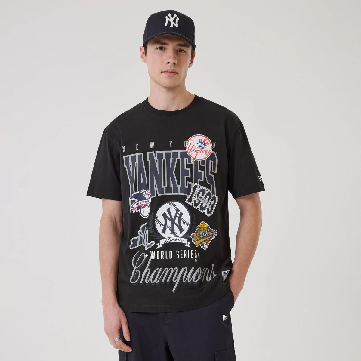New Era New York Yankees MLB Sport Classic Black T-Shirt, front view on-model featuring large grey Yankees lettering with various team patches and a World Series Champions script, complemented by a white embroidered New Era logo on the sleeve.