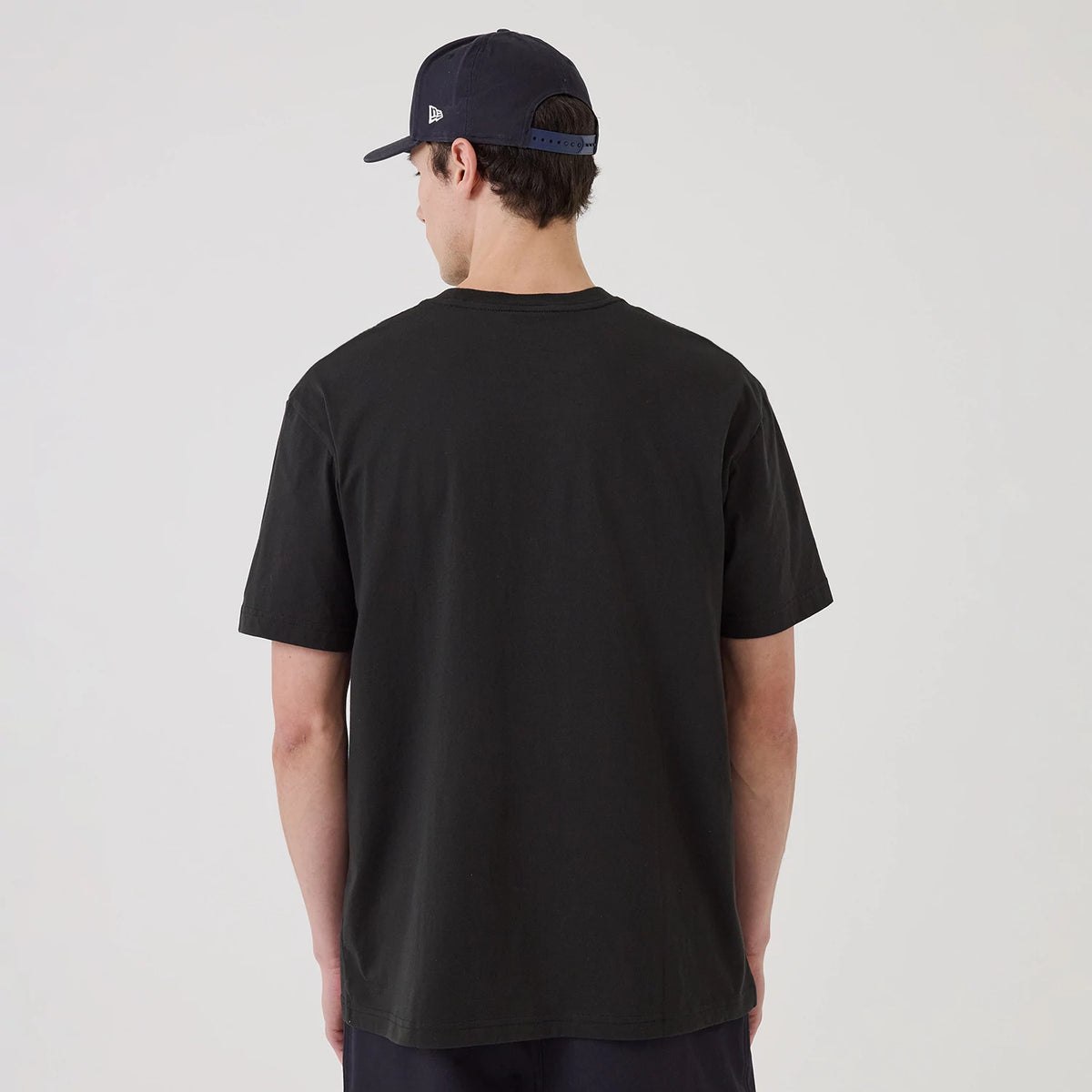 New Era New York Yankees MLB Sport Classic Black T-Shirt, back view on a model wearing a matching dark cap, showing the plain black back of the T-shirt with short sleeves and a simple round neck design.