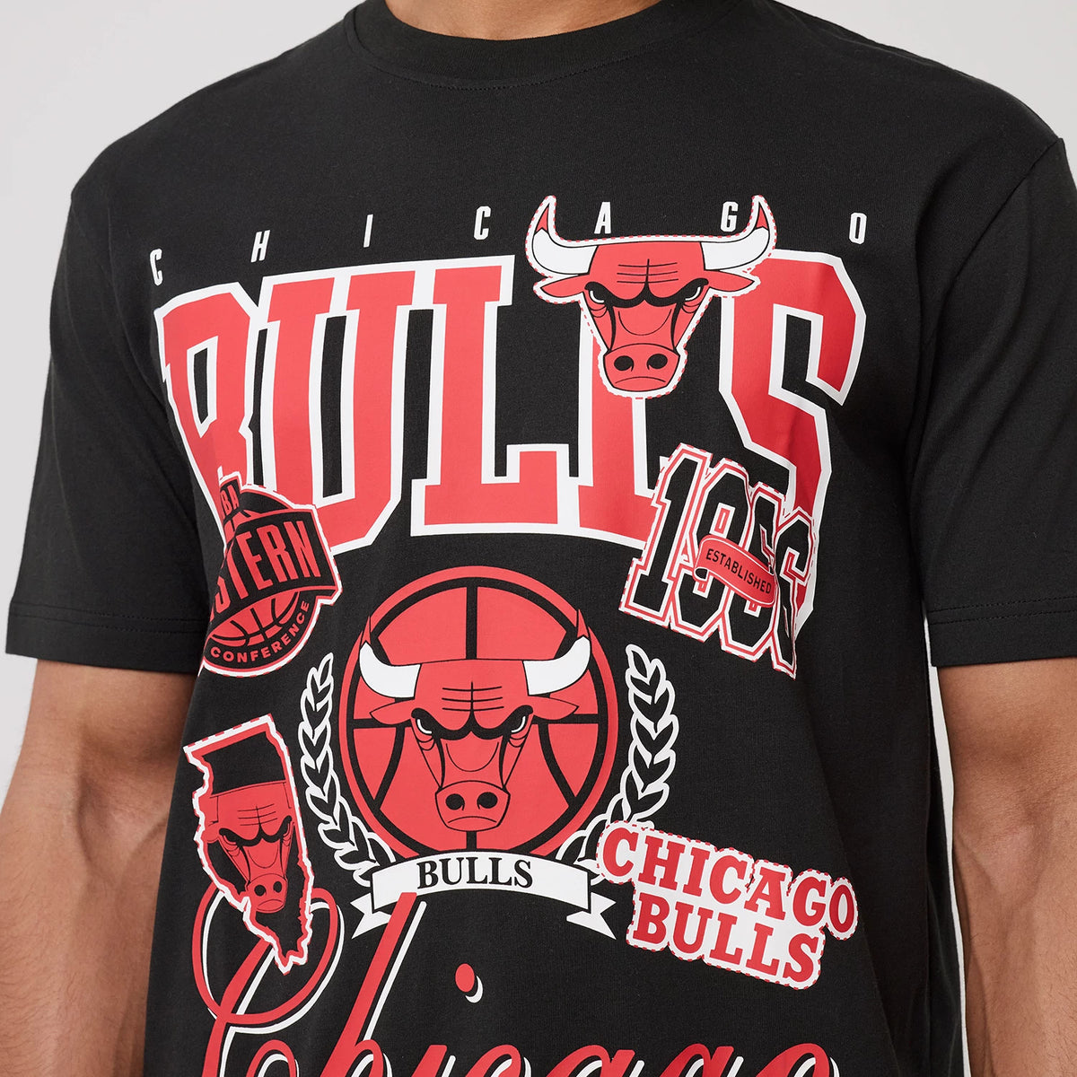 New Era Chicago Bulls NBA Sport Classic Black T-Shirt, front view with red and white Bulls logo, team emblem, and graphic patches prominently displayed across the chest, worn by a model.