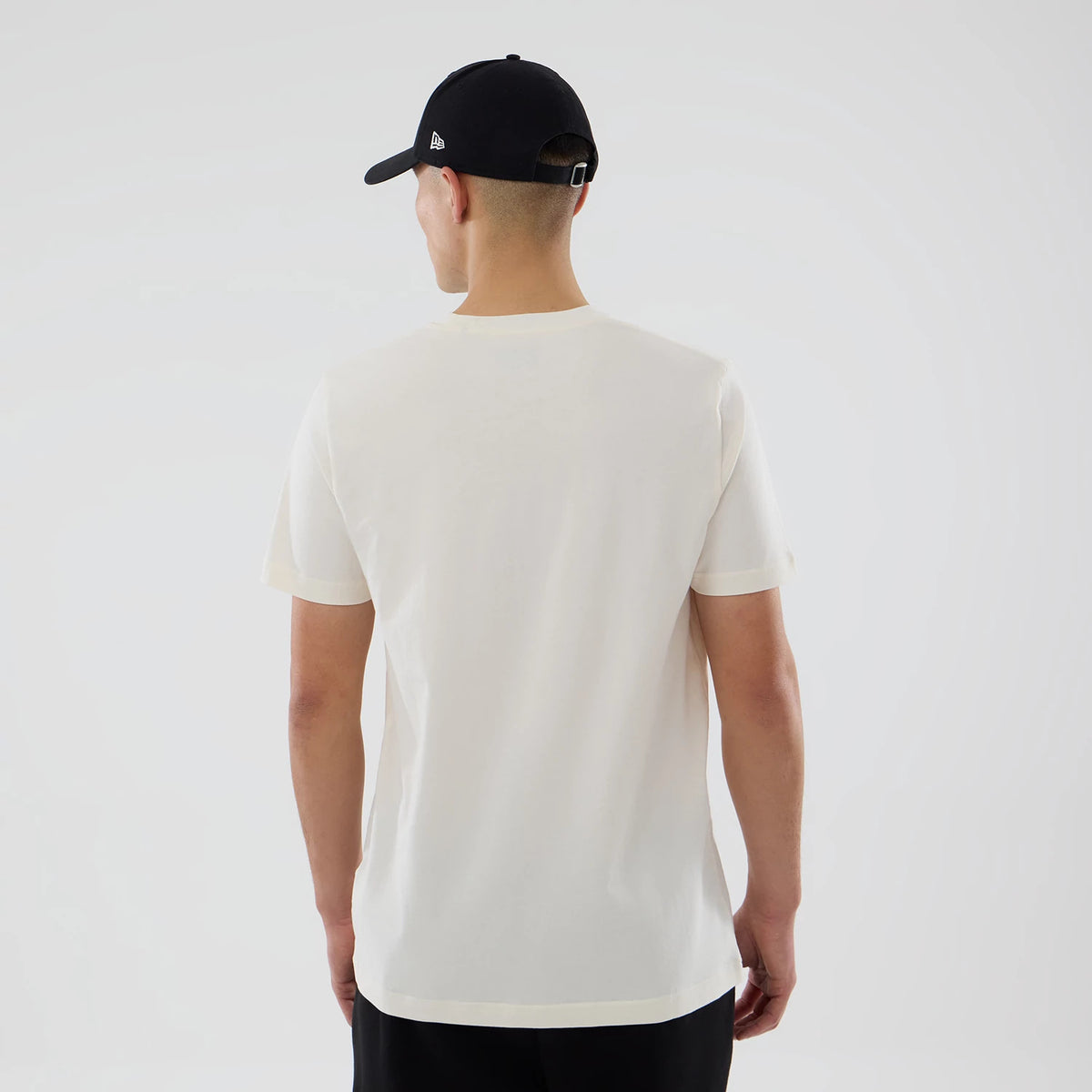 New Era Grapefruit League Logo MLB Spring Training 2026 Cream T-Shirt, back view on-model showing the plain cream back without graphics or logos, styled with a black cap that has a raised New Era logo on the side.