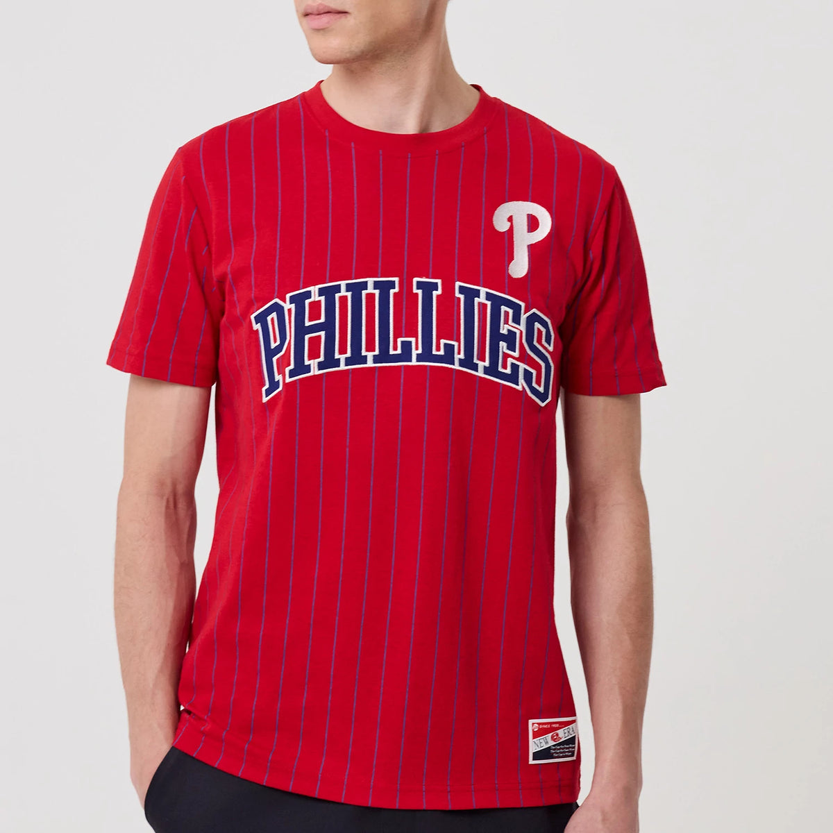 New Era Philadelphia Phillies MLB Pinstripe Red T-Shirt, front view showing a red background with vertical pinstripes, large PHILLIES lettering in blue with a white outline across the chest, and an embroidered white P logo on the upper left chest.