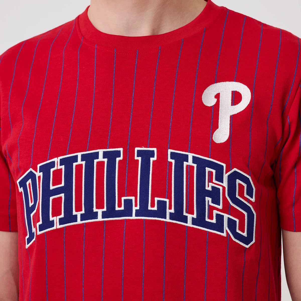 New Era Philadelphia Phillies MLB Pinstripe Red T-Shirt, front view showing vertical blue pinstripes on a red background with an embroidered white P on the left chest and PHILLIES lettering across the front in white and blue.