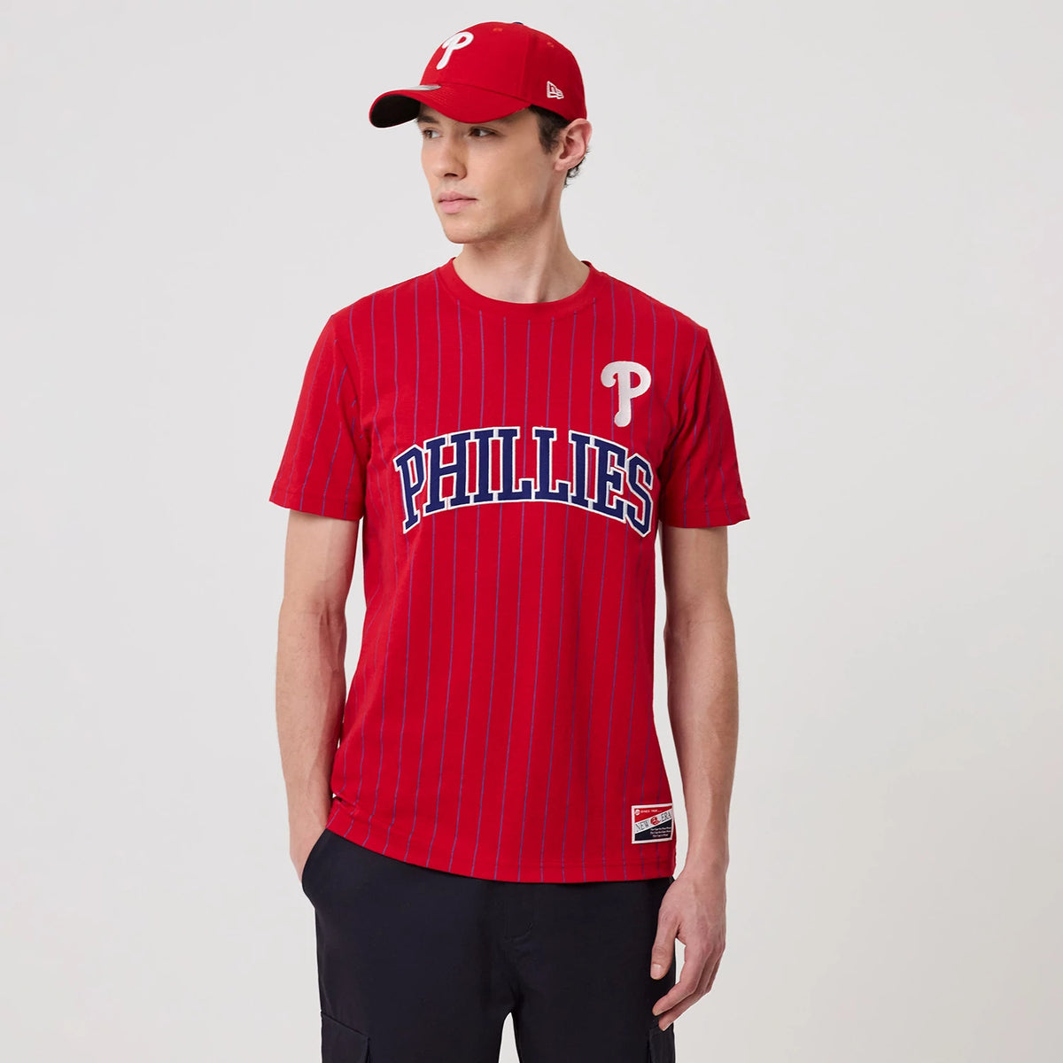 New Era Philadelphia Phillies MLB Pinstripe Red T-Shirt, front view on a model showcasing a red pinstripe design with the raised Phillies logo in blue and white across the chest and a printed New Era logo on the left sleeve.