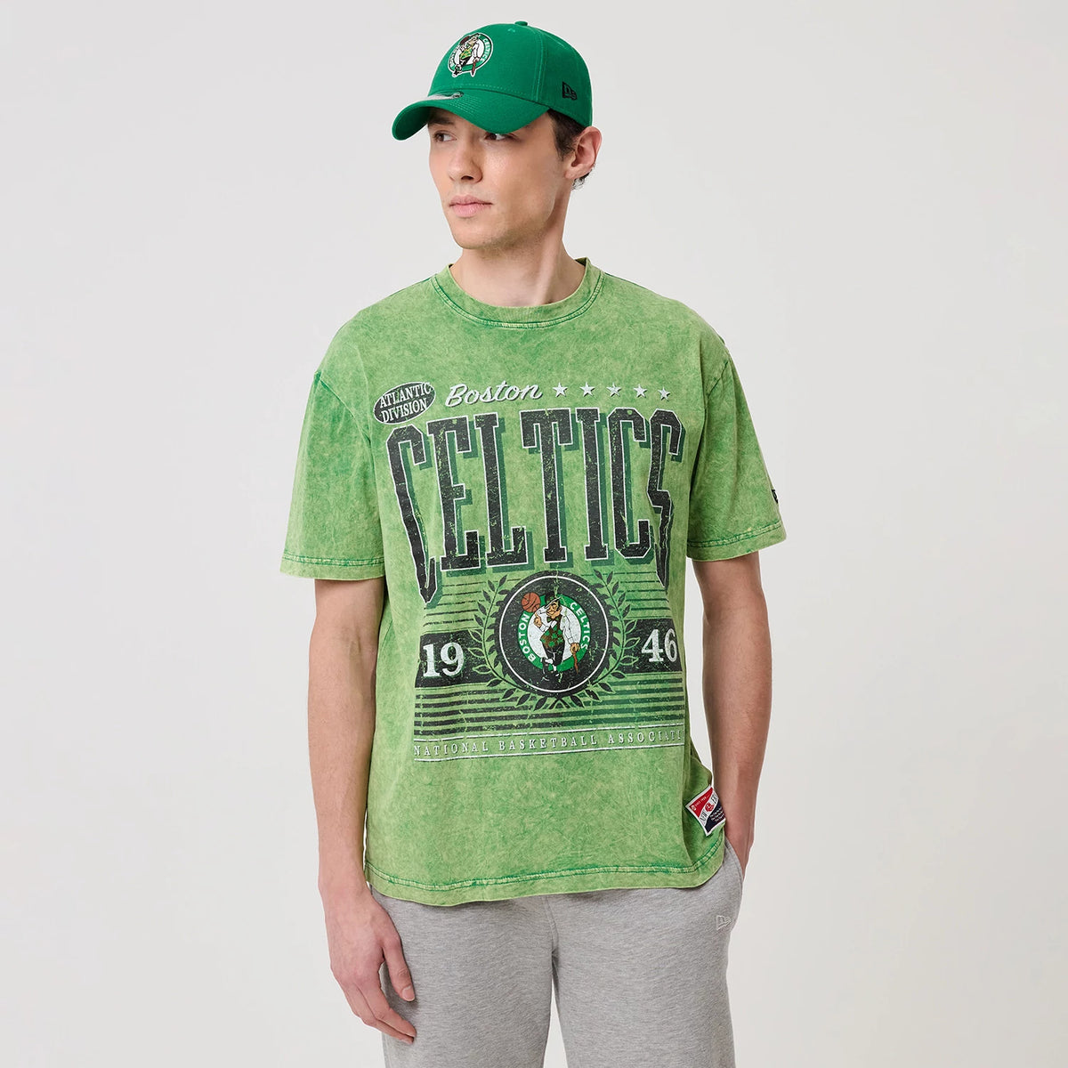 New Era Boston Celtics NBA Green T-Shirt, front view on-model featuring large distressed Celtics graphics across the chest with a printed team logo in the centre and additional text and star details above in black and white.