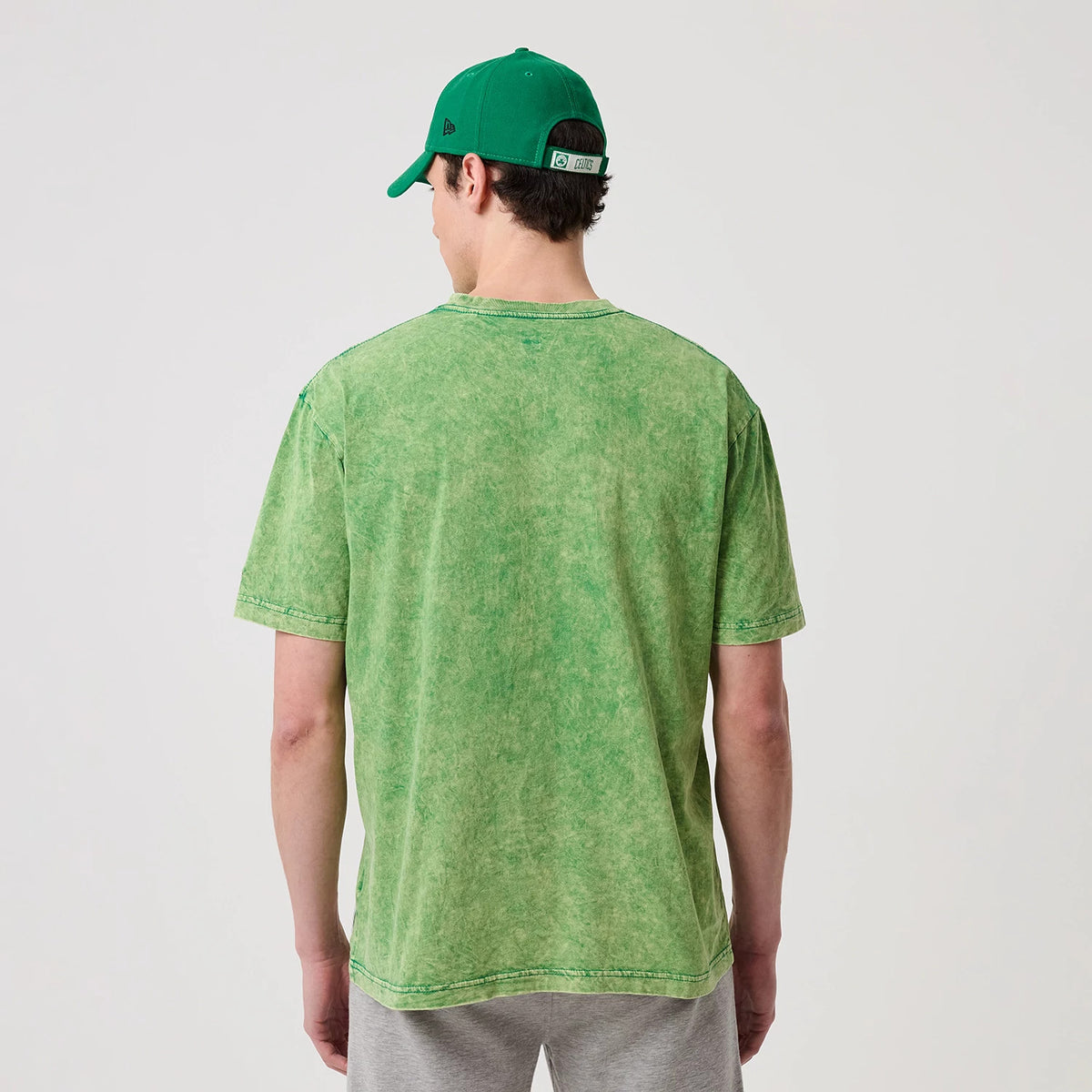 New Era Boston Celtics NBA Green T-Shirt, back view showing a plain green design with a washed effect, worn by a model also wearing a green cap, giving a casual and relaxed appearance.