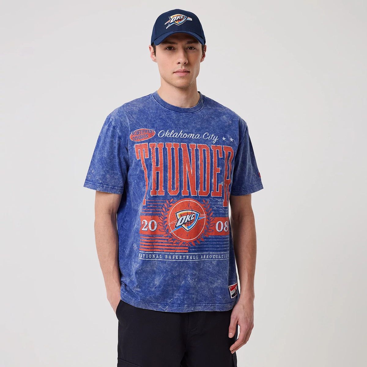 New Era Oklahoma City Thunder NBA Blue T-Shirt, front view on-model showing the large THUNDER lettering in red across the chest, the OKC logo below with 2008 and laurel graphics flanking it, worn with a matching blue cap.