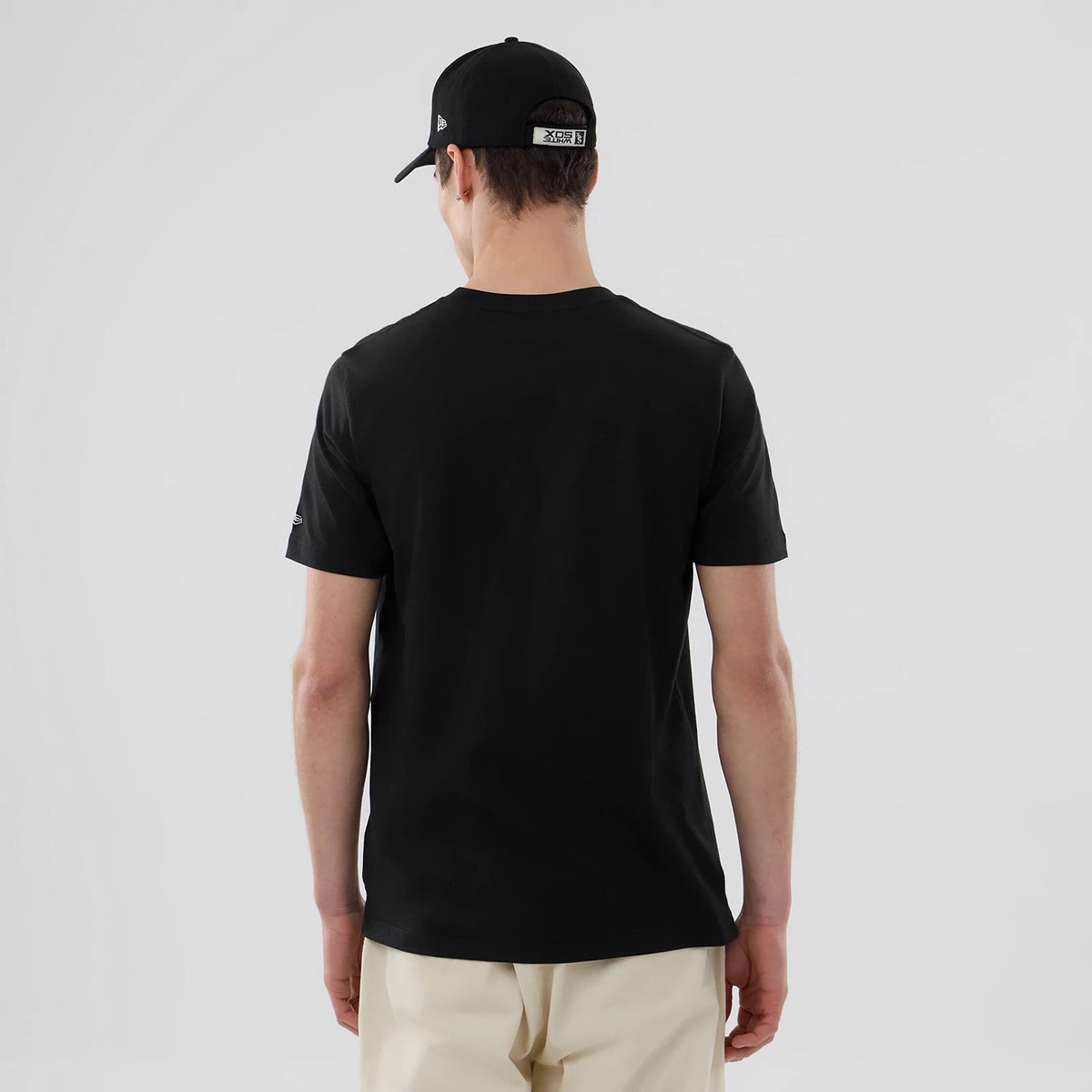 New Era Chicago White Sox MLB Popcorn Black T-Shirt, back view on-model showing a plain black surface with a small embroidered New Era logo on one sleeve, styled with a black cap and cream trousers.