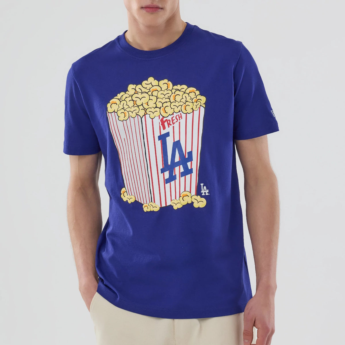 New Era LA Dodgers MLB Popcorn Dark Blue T-Shirt, front view on-model featuring a large printed graphic of an overflowing popcorn bucket with red and white stripes, an LA logo on the chest, and a small embroidered New Era logo on the sleeve.