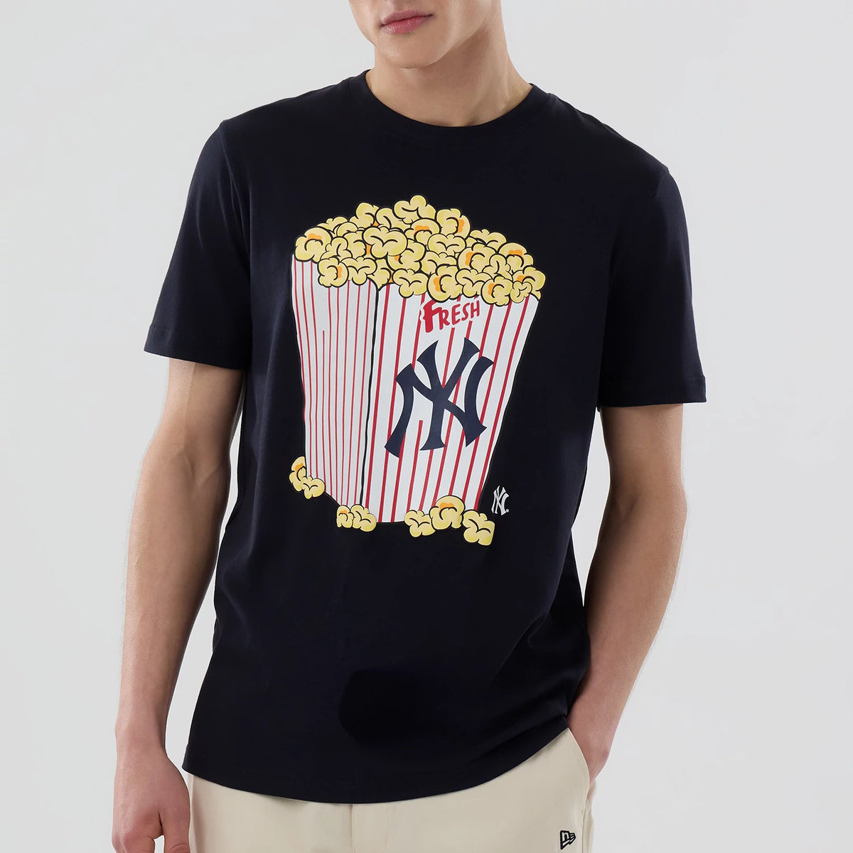 New Era New York Yankees MLB Popcorn Navy T-Shirt, front view showing a large printed graphic of a popcorn box with red stripes and the Yankees logo on the chest, worn by a model with light trousers.
