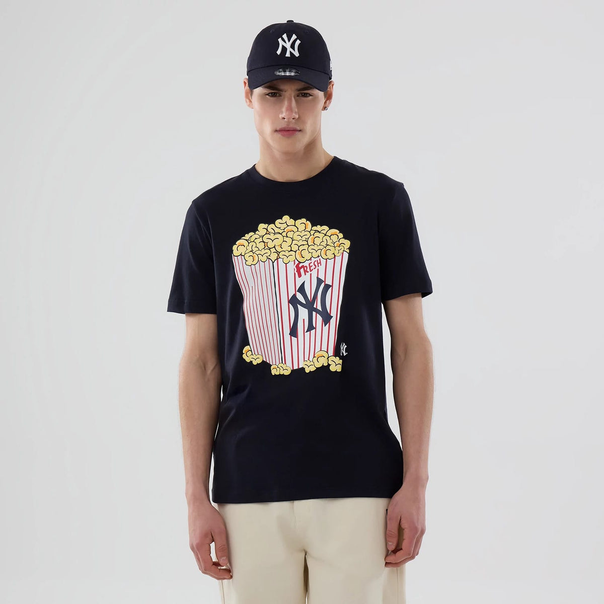 New Era New York Yankees MLB Popcorn Navy T-Shirt, front view on-model showing a large graphic of a red-and-white striped popcorn box overflowing with popcorn and the Yankees logo on the chest, paired with a matching navy cap.