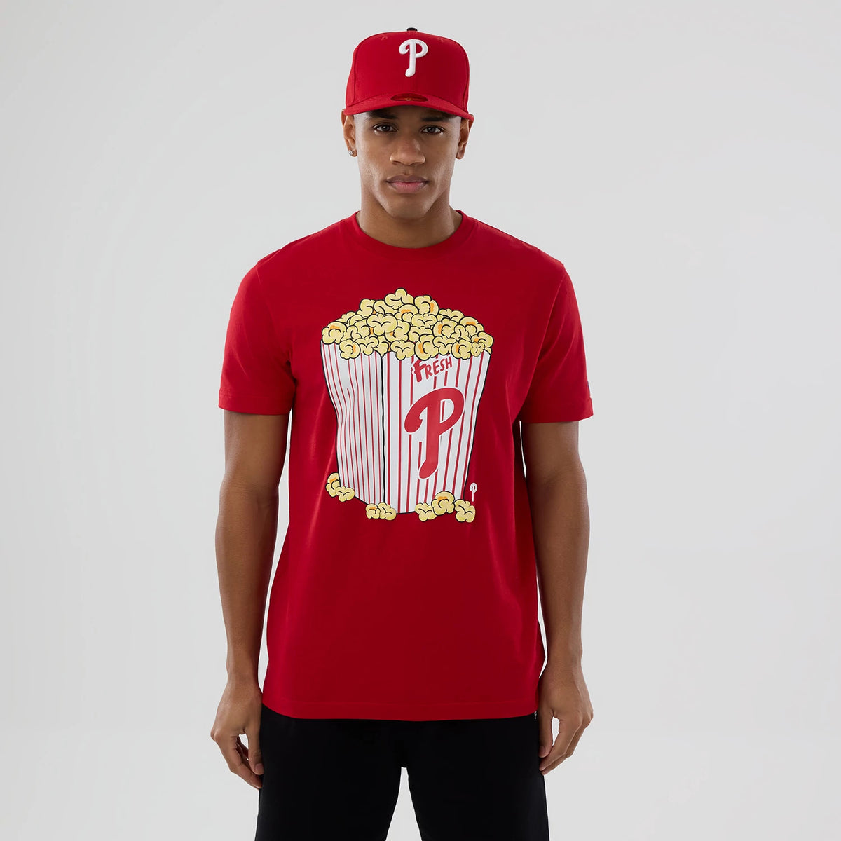 New Era Philadelphia Phillies MLB Popcorn Red T-Shirt, front view on a model styled with a matching cap, featuring a large popcorn graphic with red striped box and an embroidered P logo in the centre of the chest.