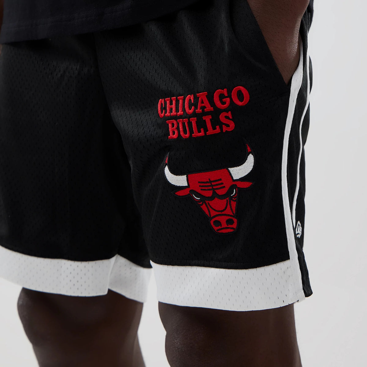 New Era Chicago Bulls NBA Black Mesh Shorts, front view showing the embroidered Chicago Bulls logo and team name in red on the left leg, with white trim at the hem and a small embroidered New Era logo near the pocket.