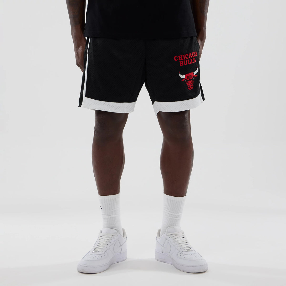 New Era Chicago Bulls NBA Black Mesh Shorts, front view on a model showing the red embroidered Chicago Bulls logo and lettering on the right leg, with white trim at the bottom and two vertical stripes on the sides.