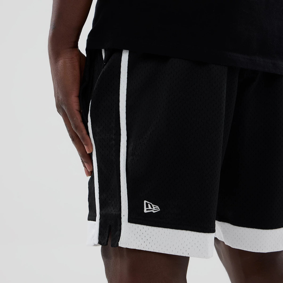 New Era Chicago White Sox MLB Black Mesh Shorts, side view showing black mesh fabric with white side stripes and hems, an embroidered New Era logo above the left hem, worn by a model with a black top.