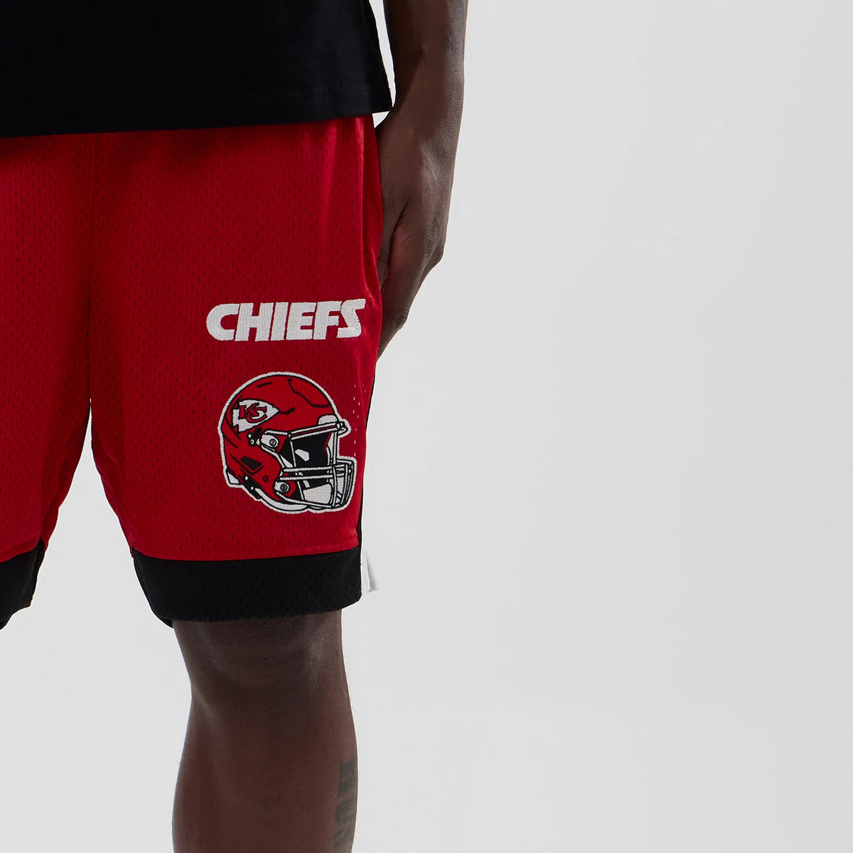 New Era Kansas City Chiefs NFL Red Mesh Shorts, front view showing the red mesh fabric with a printed Chiefs helmet logo and white CHIEFS lettering on one leg, complemented by contrasting black trim at the hem.