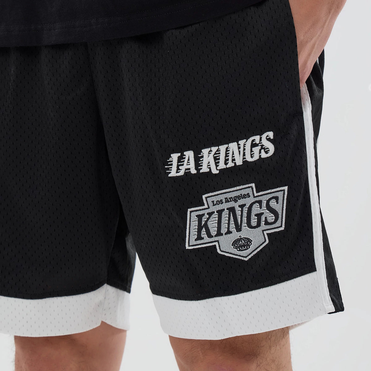 New Era LA Kings NHL Black Mesh Shorts, front view on-model showing LA Kings embroidered in white above the Los Angeles Kings logo on the right leg, with contrasting white trim and mesh throughout.