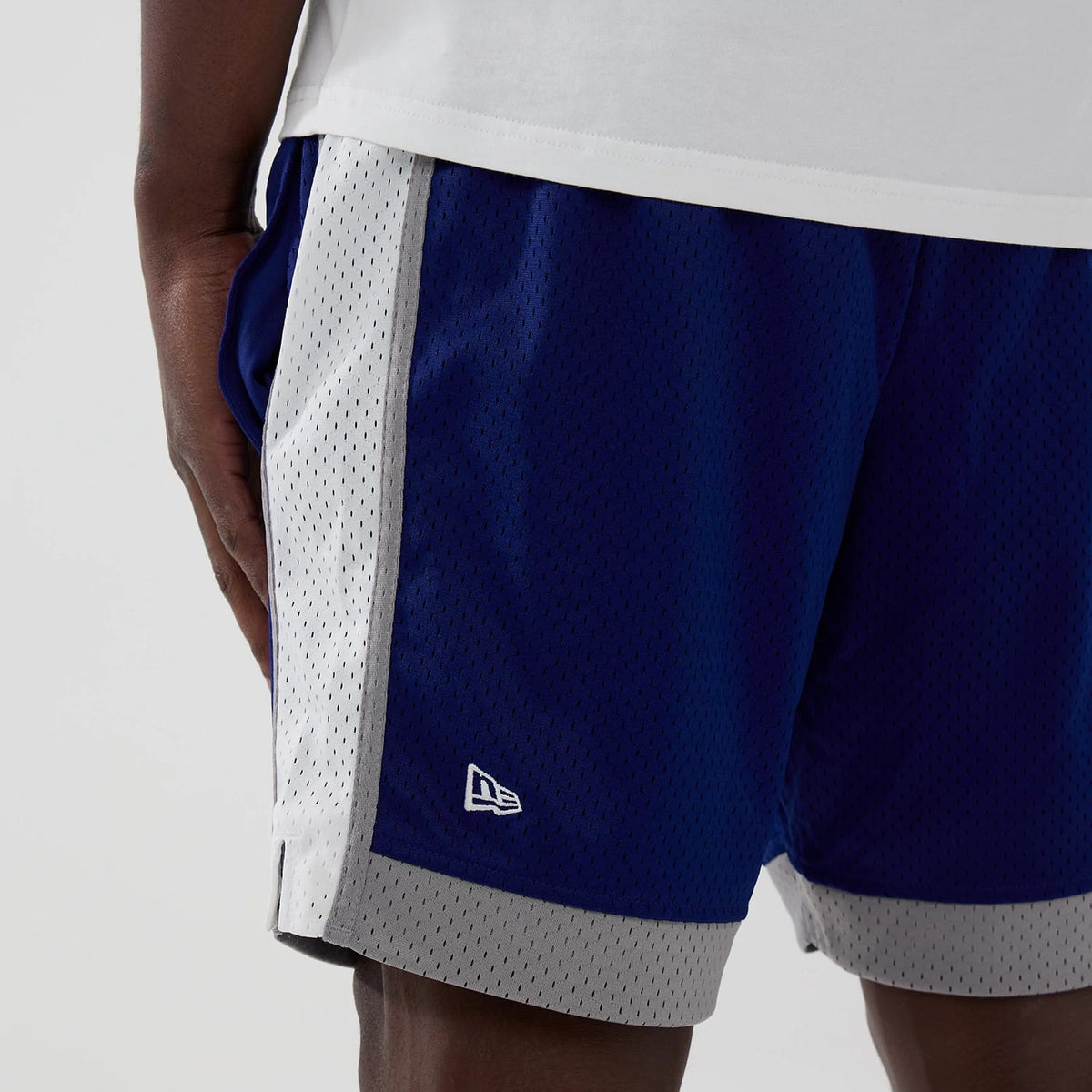 New Era LA Dodgers MLB Dark Blue Mesh Shorts, three-quarter view showing dark blue shorts with a light grey panel on the side, an embroidered New Era logo near the hem on the left side, and perforations throughout for a mesh style.