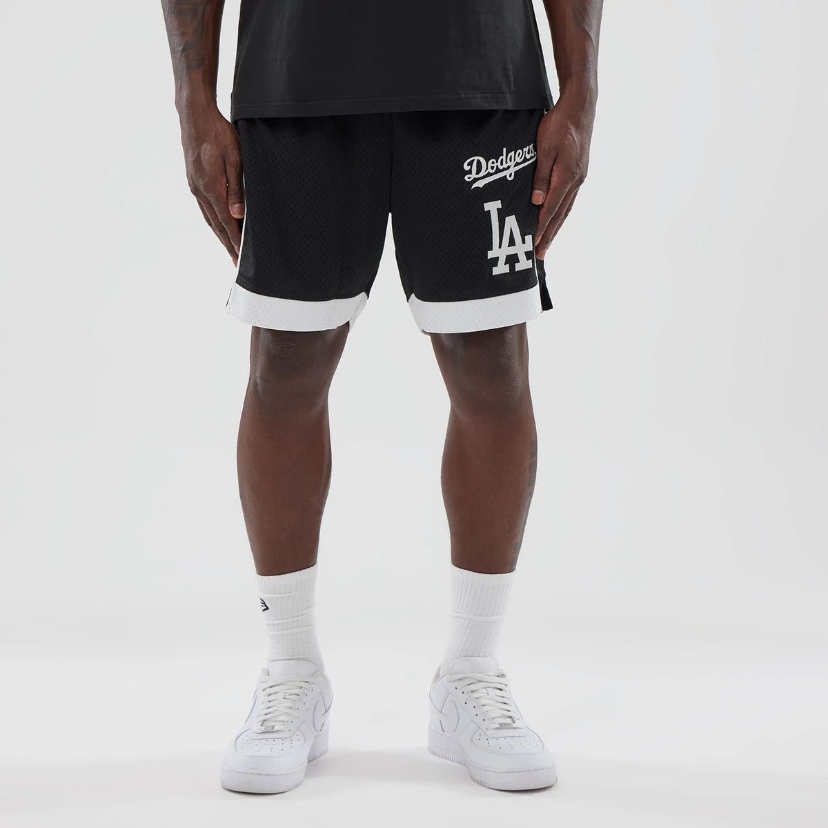 New Era LA Dodgers MLB Black Mesh Shorts, front view on-model showing the black shorts with white trim, an embroidered Dodgers script logo on the left and a large LA logo beneath it near the hem.
