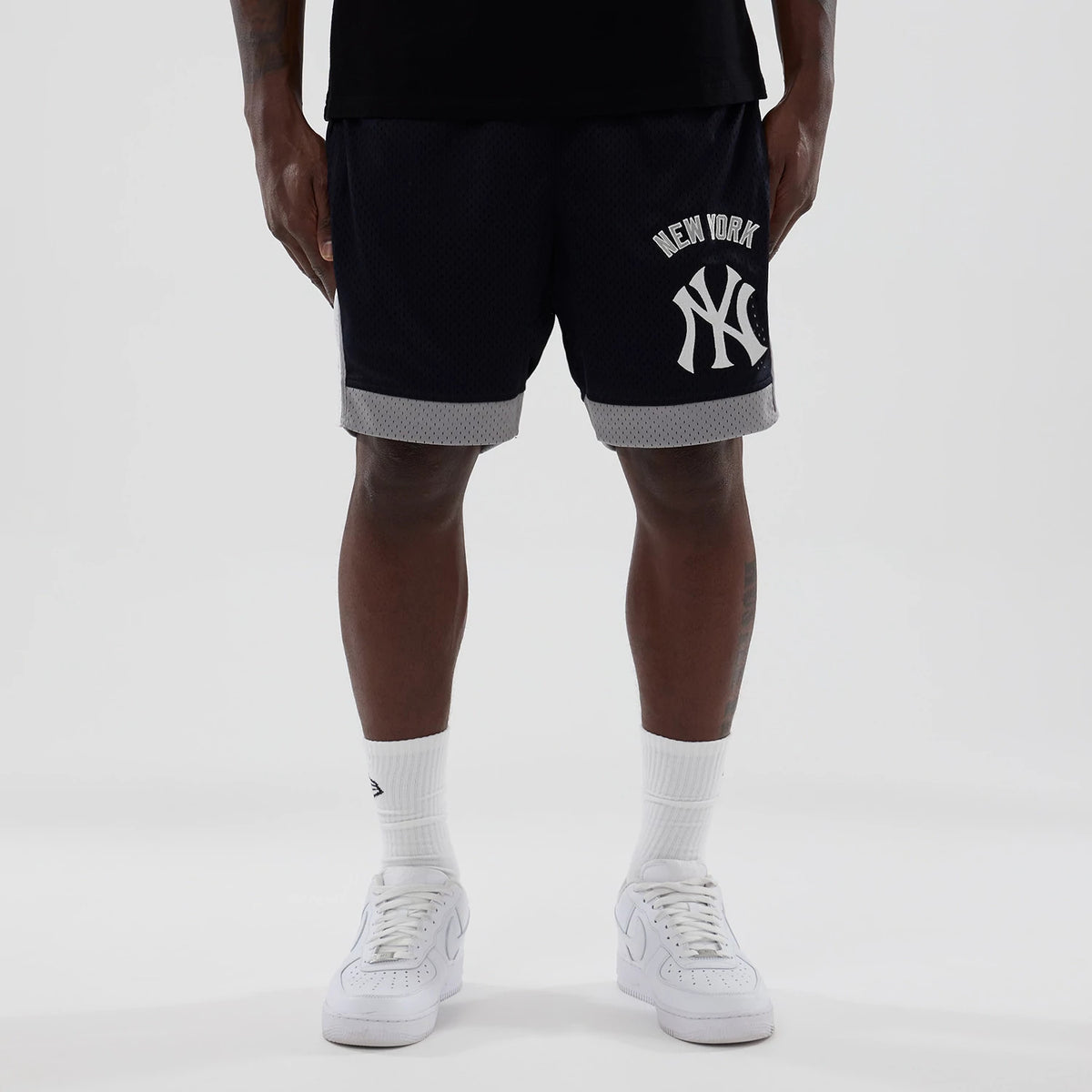 New Era New York Yankees MLB Navy Mesh Shorts, front view showing the large white embroidered Yankees logo on the left leg, grey trim at the hem, styled on-model with white trainers and a black top.