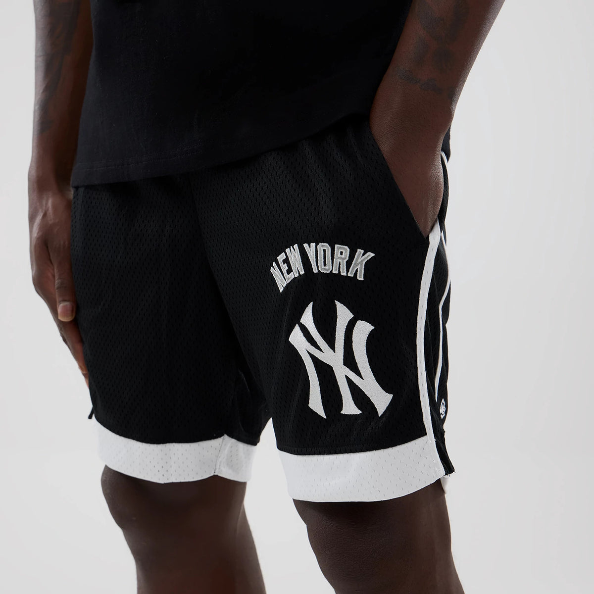 New Era New York Yankees MLB Black Mesh Shorts, front view on-model showing the white embroidered New York lettering and Yankees logo on the left leg, black mesh fabric with white trim at the hem and white side stripes.