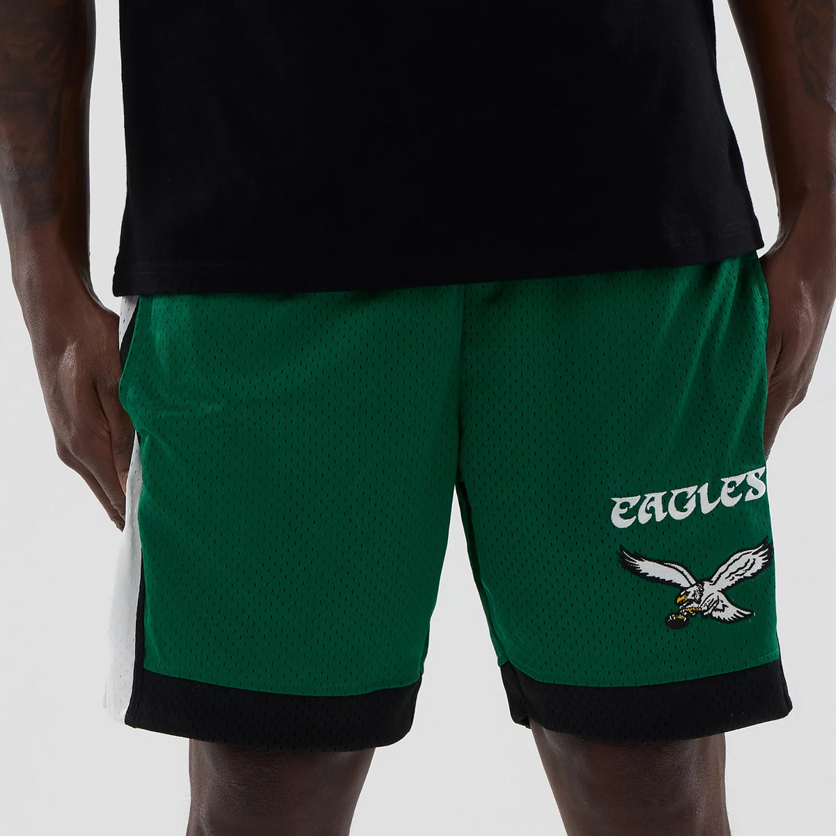 New Era Philadelphia Eagles NFL Green Mesh Shorts, front view on-model showing Eagles wording in white above an embroidered team logo on the lower right leg, with contrasting black and white side panels and a loose fit.