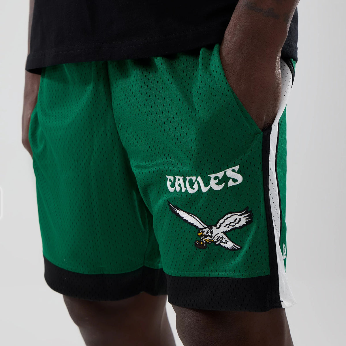 New Era Philadelphia Eagles NFL Green Mesh Shorts, front three-quarter view showing the white embroidered Eagles logo and text on the left leg, with white side stripes and black trim at the hem.
