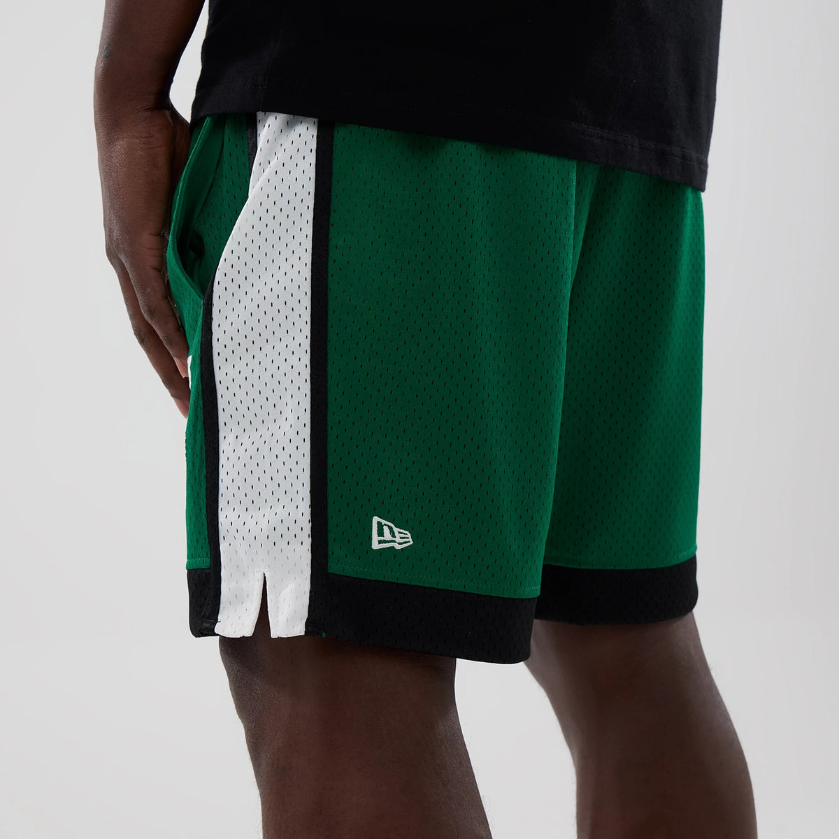 New Era Philadelphia Eagles NFL Green Mesh Shorts, three-quarter view showing the green fabric with a white side stripe, an embroidered New Era logo near the hem, and black trim at the bottom, styled on a model with a black top.