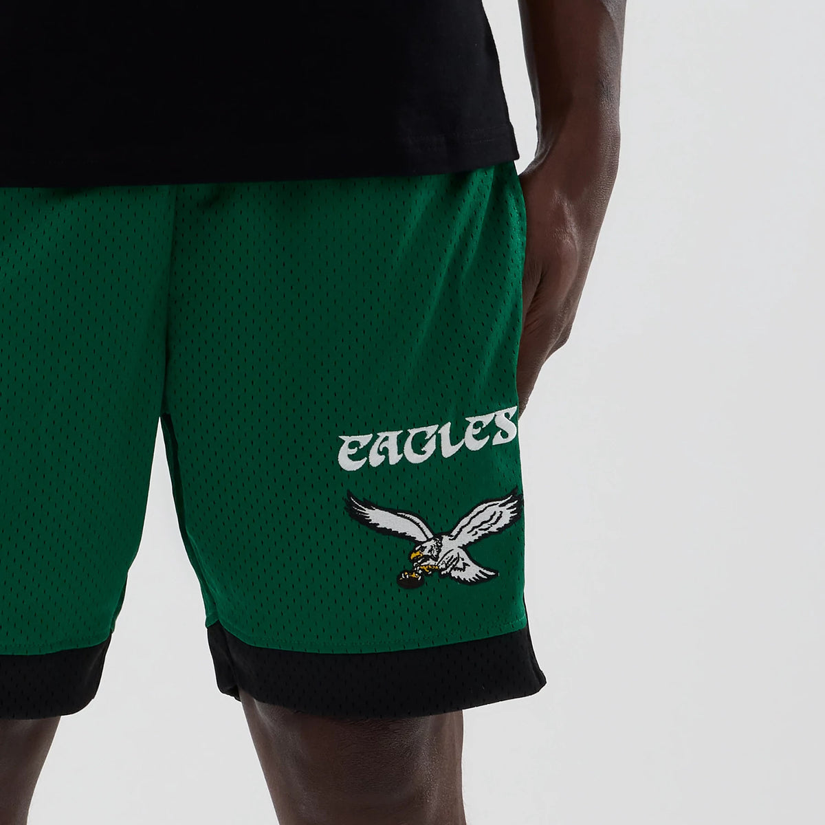 New Era Philadelphia Eagles NFL Green Mesh Shorts, front view showing the green mesh fabric with black trim at the hem, an embroidered Eagles logo with a flying eagle near the left hem, and Eagles lettering in white above.