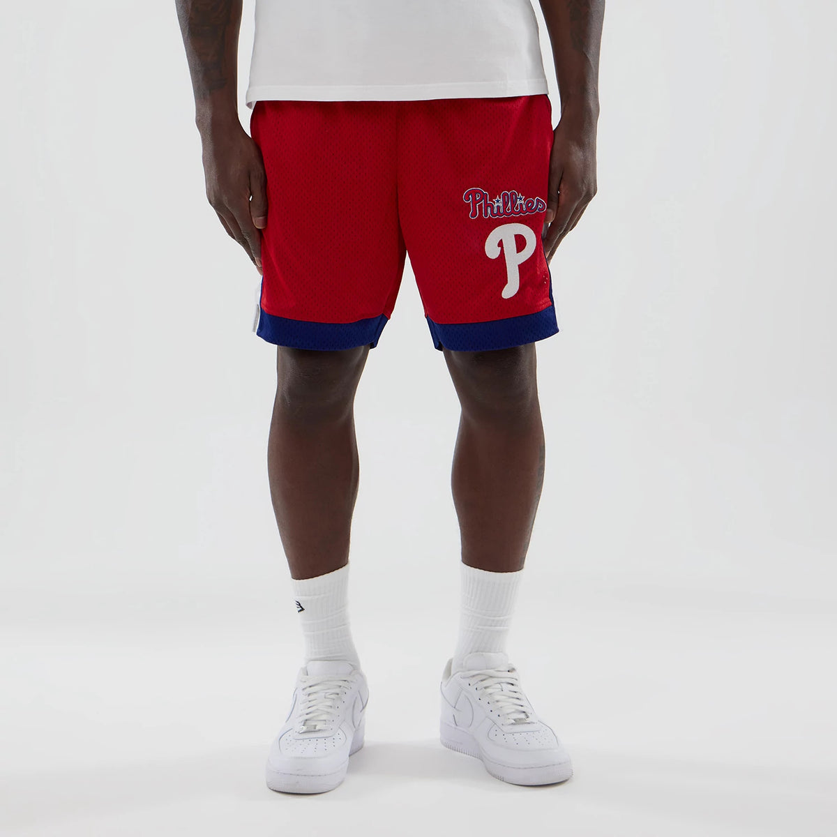 New Era Philadelphia Phillies MLB Red Mesh Shorts, front view on a model showing the bright red mesh fabric with a raised Phillies script logo and an oversized P on one leg above a blue band around the hem.