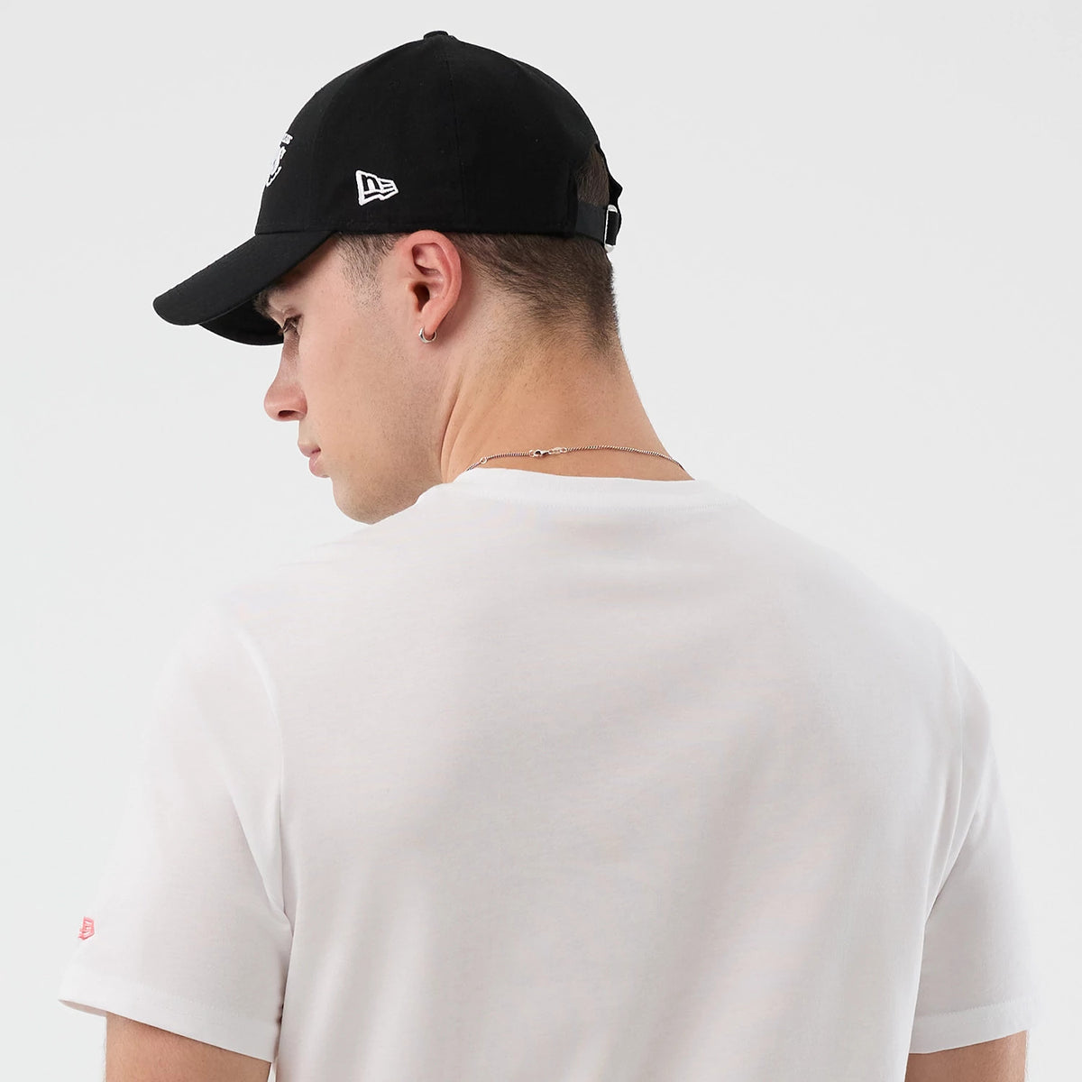 New Era LA Lakers NBA Back To School Graphic White T-Shirt, back view on-model showing a plain white back and short sleeves, paired with a black cap featuring an embroidered New Era logo on the side.