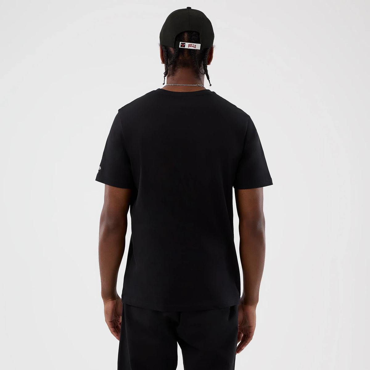 New Era Chicago Bulls NBA Back To School Black T-Shirt, back view on a model wearing a matching black cap, showing a plain back with short sleeves and an embroidered New Era logo on the left sleeve.