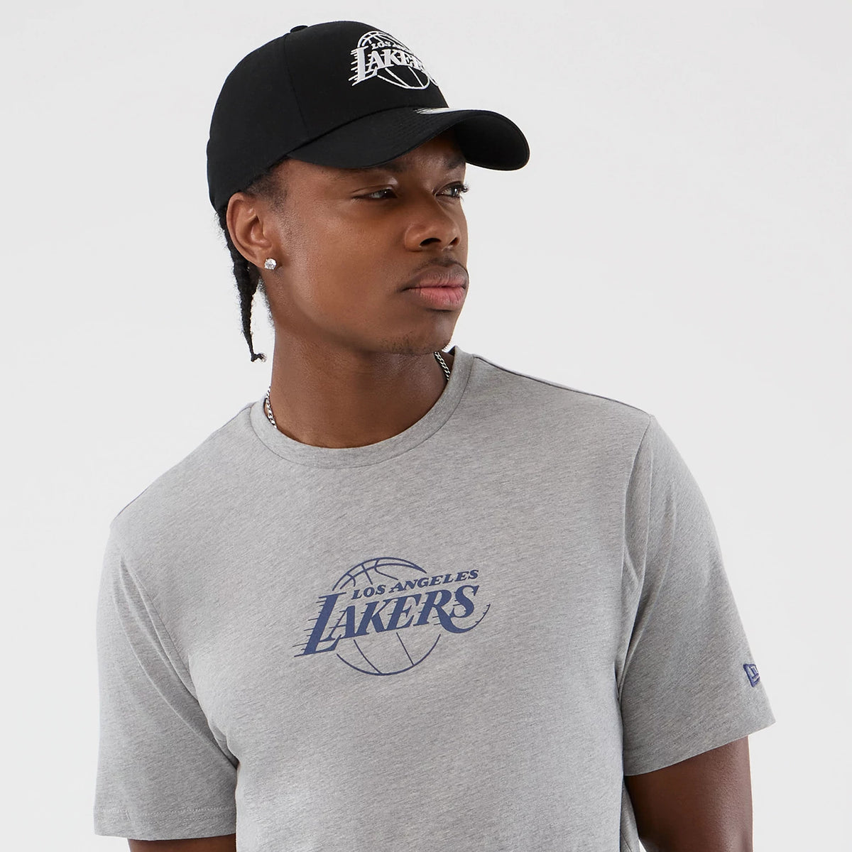 New Era LA Lakers NBA Back To School Grey T-Shirt, front view on model with a black cap, displaying the blue Los Angeles Lakers logo printed centrally on the chest and a small embroidered New Era logo on the sleeve.