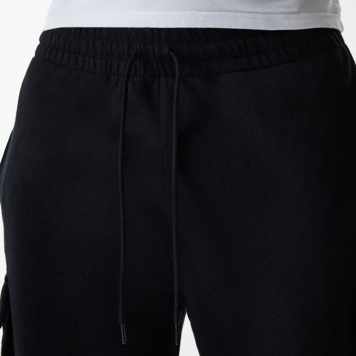 New Era Black Cargo Joggers, front view showing the elasticated waistband with black drawstrings and the upper part of the left leg with pocket seams, featuring a relaxed fit and a plain black design.