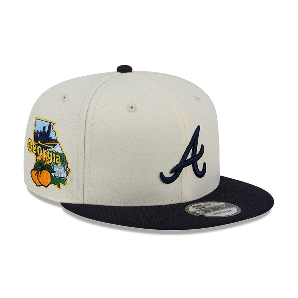 Atlanta Braves MLB Localized White New Era 9FIFTY Snapback Adjustable Cap, three-quarter view showing a navy blue embroidered A logo on the front panel, with a navy visor and a 9FIFTY size sticker, and colourful Georgia patch on the side.